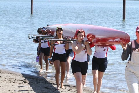 A junior girls eight walks their boat up a launch area. 