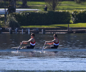 Two rowers are pictured rowing on a lake