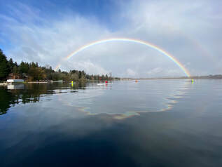A rainbow appears over Lake Sammamish while several single boats are rowing on the lake. 