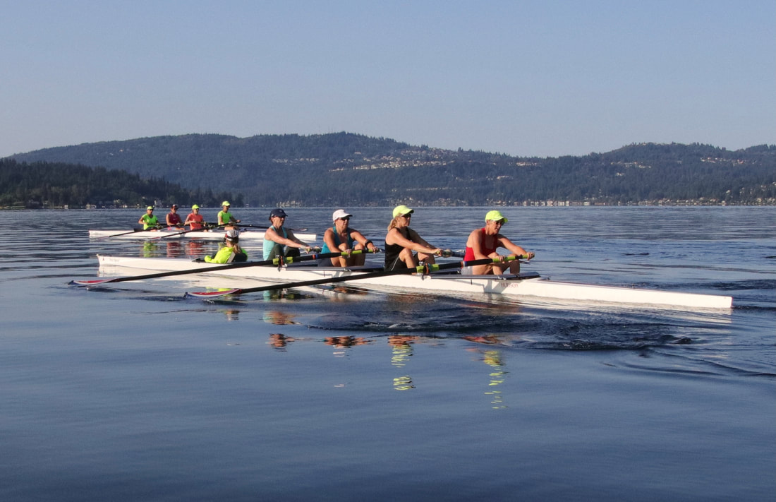 Two masters quads are pictured on Lake Sammamish on a sunny day. The rowers wear bright colors. 
