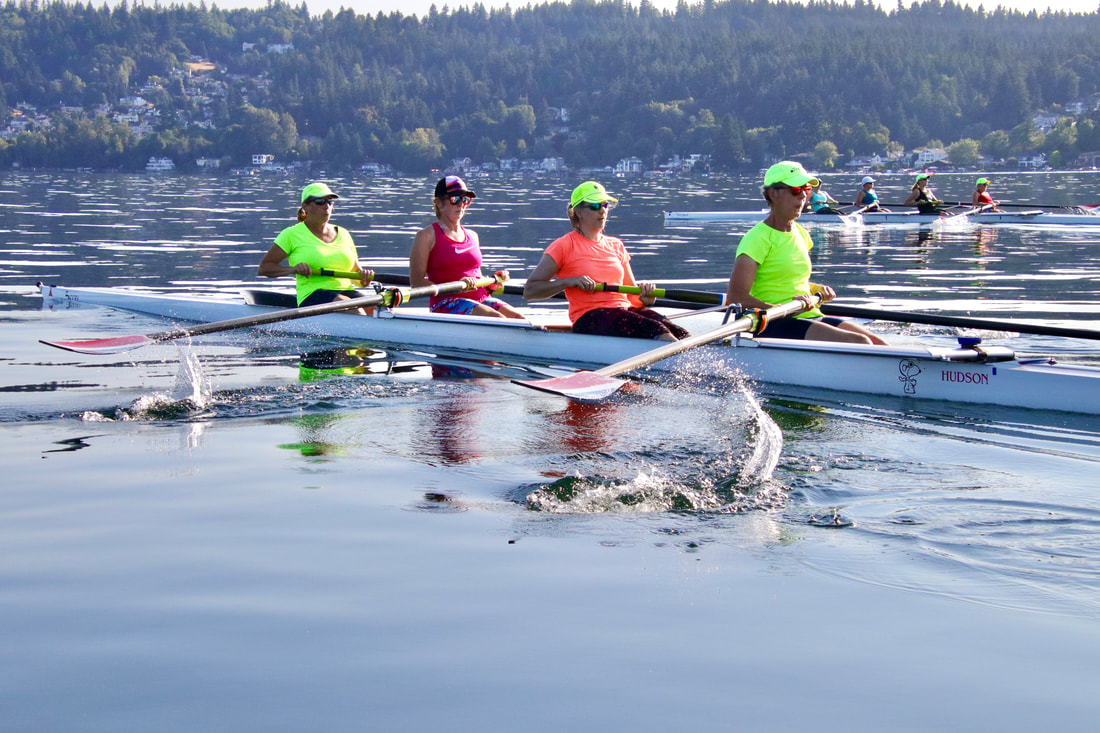 Two fours row on Lake Sammamish. The rowers are in bright colors. 