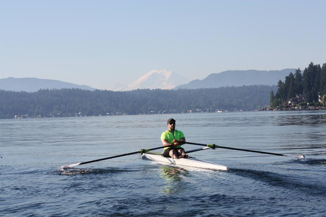 A single with a man wearing a neon yellow shirt is on Lake Sammamish with Mount Rainier in the background.