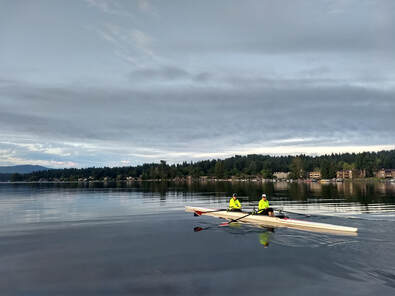 A double sits on Lake Sammamish with grey skies above. The two rowers wear neon yellow shirts and stand out in the grey water.